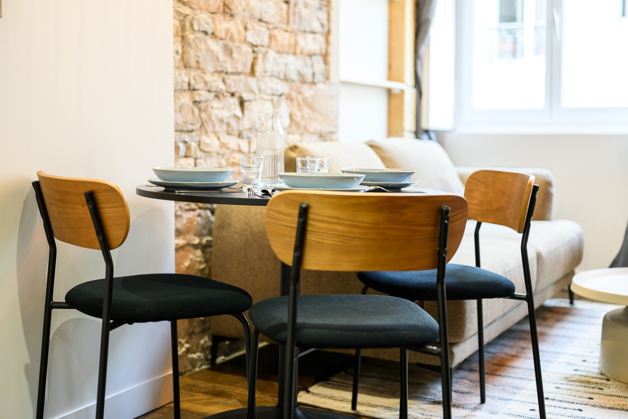 c'est une coin repas avec une table ronde et des chaises noires et bois