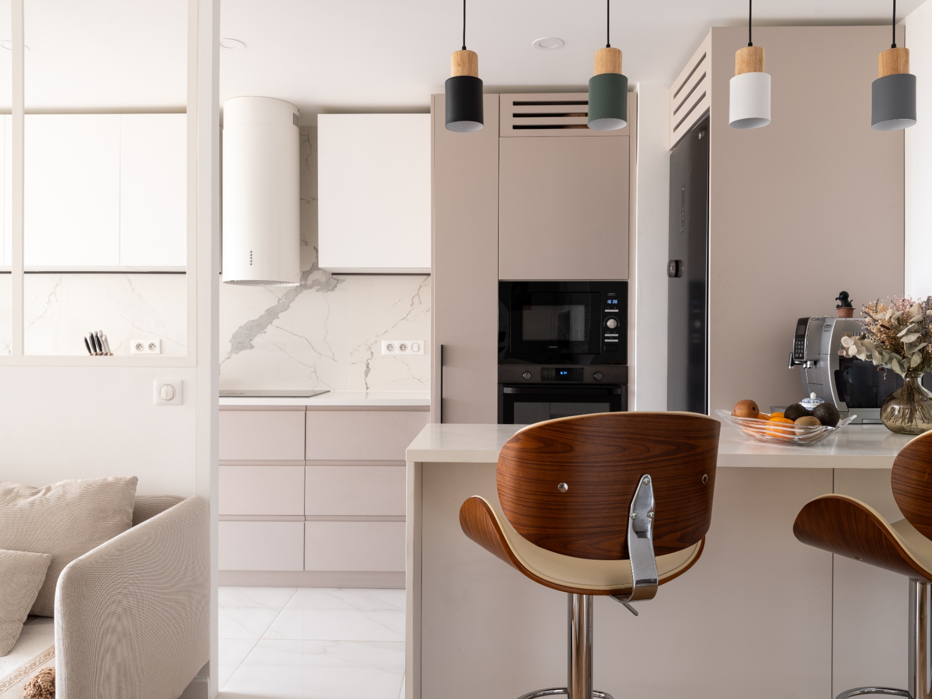 Cuisine contemporaine et minimaliste avec îlot central, meubles aux tons beige et blanc, électroménager intégré, suspensions design et tabourets en bois, dans un espace lumineux et épuré.